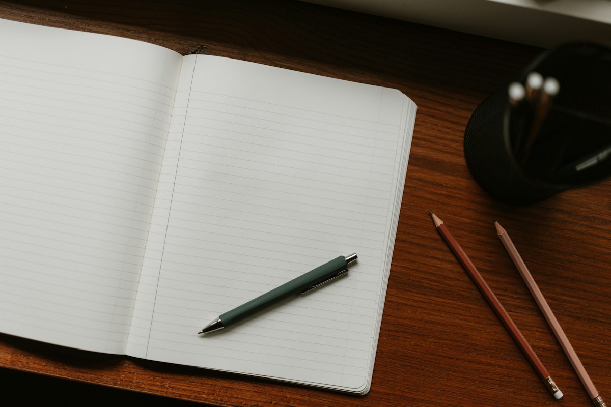 An open notebook, pen and pencils on a wooden desk.